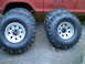 1979 Ford Bronco - Four off-road tires and wheels are displayed next to the red body of a vehicle.