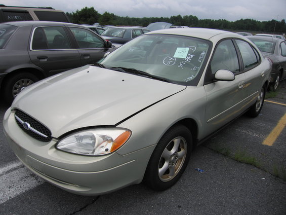 Silver sedan with hood slightly ajar, parked in a lot with other cars. Windshield has writing on it