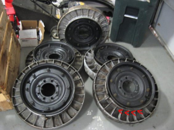 Several large vehicle wheels with metal fins around the rim are stacked on a concrete floor