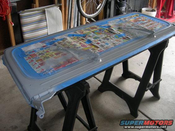 Gray car door taped and covered with newspaper, resting on sawhorses