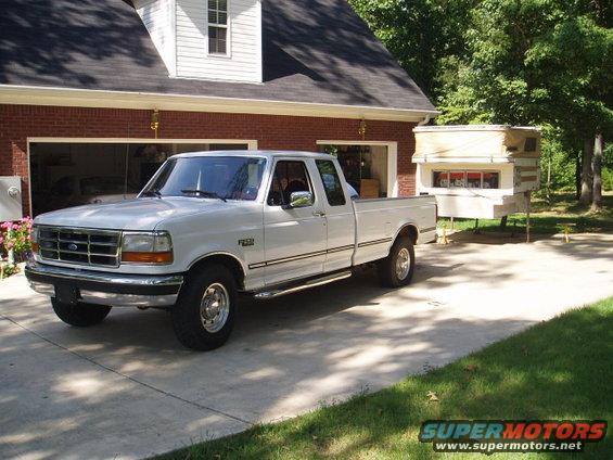 White Ford F-250 pickup truck parked in driveway, with a camper unit mounted in the bed. House in background