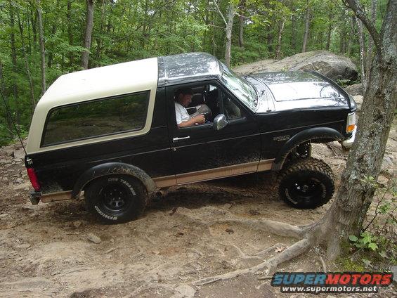 Black 1995 Ford Bronco with a white top driving on a rocky trail