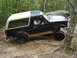1995 Ford Bronco - A driver navigates a black Ford Bronco with a two-tone top over a challenging, wooded off-road course.