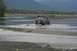 1990 Chevrolet Suburban - A Jeep Cherokee XJ navigates a shallow riverbed, with another vehicle visible in the distance.