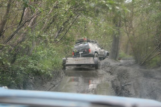 Black SUV towing a trailer through mud and trees