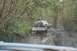 1990 Chevrolet Suburban - A black SUV navigates a muddy path, towing a trailer through a wooded area.