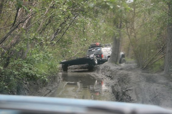 Off-road vehicle towing a trailer through a muddy trail with trees on both sides