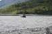 1990 Chevrolet Suburban - An SUV tows a trailer through a shallow, fast-moving river in a mountainous, forested area.