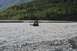1990 Chevrolet Suburban - A black SUV navigates a shallow, rocky river with a forested mountainside behind it.