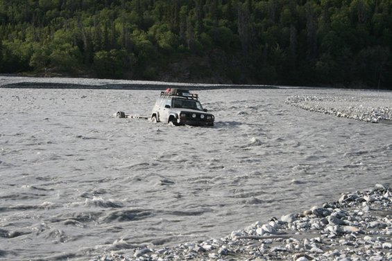 Silver SUV being towed through a shallow river, trailer attached