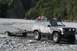 1990 Chevrolet Suburban - A muddy Jeep Cherokee XJ navigates a rocky stream bed while towing a trailer.