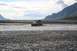 1990 Chevrolet Suburban - SUV navigates a river in a mountainous, rocky landscape under a cloudy sky.
