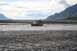 1990 Chevrolet Suburban - An off-road vehicle navigates a wide, shallow river under a cloudy sky with mountains in the distance.
