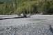 1990 Chevrolet Suburban - SUV towing a trailer through a shallow riverbed with trees in the background.