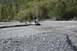 1990 Chevrolet Suburban - A gray SUV tows a trailer through a shallow, rocky river, with a dense forest lining the bank.