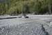 1990 Chevrolet Suburban - A gray SUV navigates a rocky riverbed, with trees lining the banks in the distance.