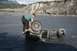 1990 Chevrolet Suburban - A man struggles to right an overturned ATV in a shallow river with mountains in the background.