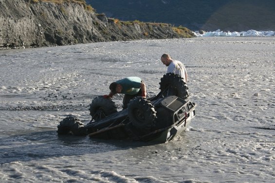 ATV overturned in shallow river with two people nearby