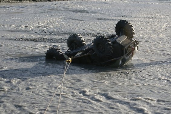 ATV overturned in muddy water, being towed by a rope