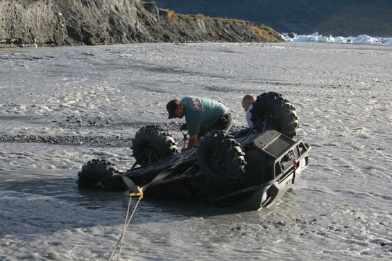 ATV on its side in a river with two people attempting recovery