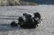 1990 Chevrolet Suburban - Two individuals work to recover an ATV that has overturned in a shallow, rocky riverbed.