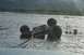 1990 Chevrolet Suburban - An off-road vehicle is stuck in a river, with shovels and a bucket on the bank.