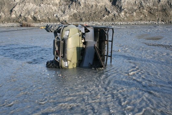 ATV flipped on its side in a shallow, rocky river, being pulled by a cable