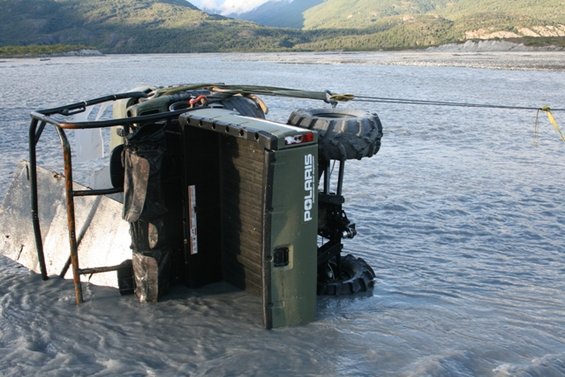 Olive green Polaris ATV on its side in shallow water, being towed