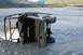 1990 Chevrolet Suburban - An olive green Polaris ATV is overturned and partially submerged in a river, with a tow rope attached.