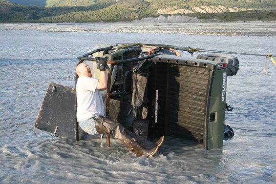 Man in water trying to pull an overturned Polaris ATV out of a river