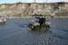 1990 Chevrolet Suburban - Two vehicles navigate a shallow, rocky riverbed under a steep, eroded embankment.