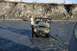 1990 Chevrolet Suburban - An ATV is being towed through a shallow river with a steep embankment in the background.