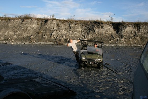 Green utility vehicle in shallow water being pulled by another vehicle