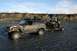 1990 Chevrolet Suburban - A Jeep Cherokee and a utility vehicle on a trailer navigate a rocky, shallow riverbed under a partly cloudy sky.