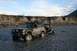 1990 Chevrolet Suburban - A modified Jeep Cherokee navigates a rocky riverbed, pulling a trailer carrying an ATV.