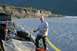 1990 Chevrolet Suburban - A man stands on a rocky shore, holding a yellow recovery strap near a vehicle.