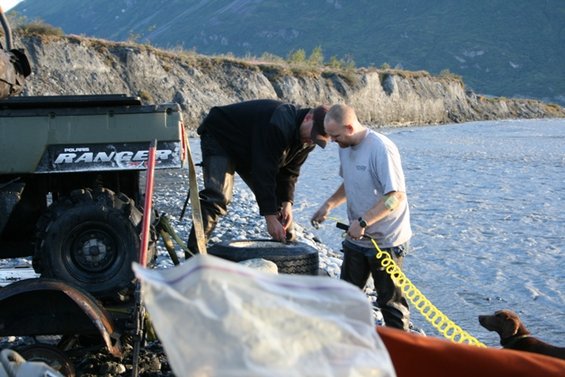 Green Polaris Ranger ATV with 'RANGER' text, rear wheel visible, on rocky shore