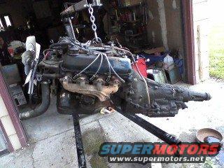 Engine and transmission assembly suspended from a hoist on a stand in a garage