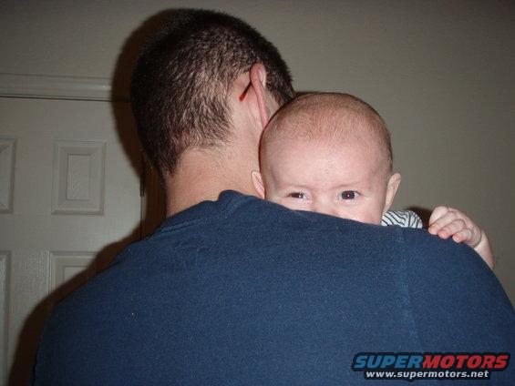 Baby peeking over a person's blue shirt shoulder, with a door in the background