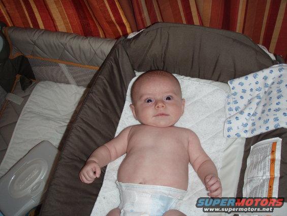 Baby in a diaper lying in a crib with striped curtains in the background
