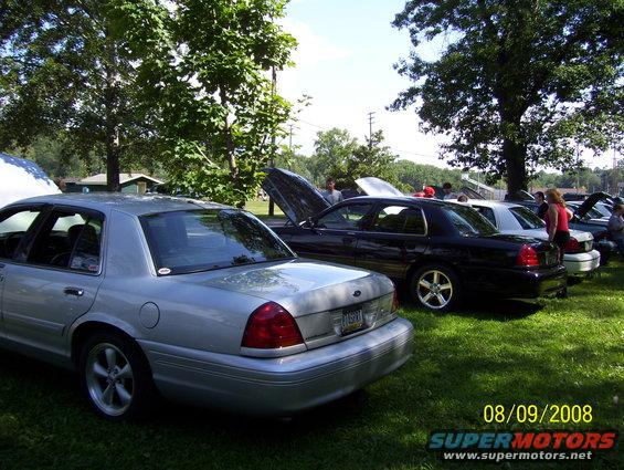 Silver and black Ford Crown Victorias parked on grass, with hoods up. Date stamp reads 08/09/2008