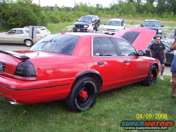 Red 2008 Ford Crown Victoria with black wheels and spoiler, hood open, parked on grass