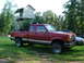 1984 Ford Bronco II - A red Ford Ranger pickup truck is parked in a yard with a treehouse and other vehicles nearby.