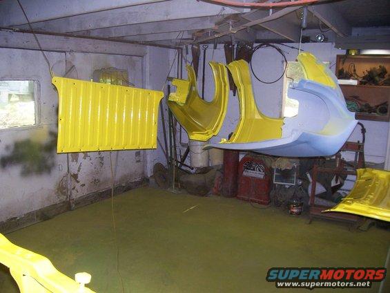 Yellow car body panels hanging in a workshop, some with primer