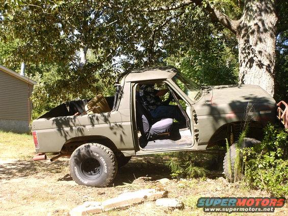 Olive green 1980 Ford Bronco with open driver's door and person inside, parked outdoors