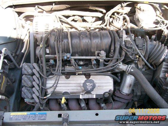 Engine bay with V6 engine components visible, including spark plug wires, intake manifold, and alternator
