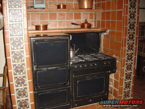Antique black stove set into a tiled alcove with copper pots on shelves above