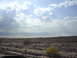 2001 Ford Mustang - A wide shot of a dry, rocky desert landscape with mountains on the horizon and a cloudy sky above.