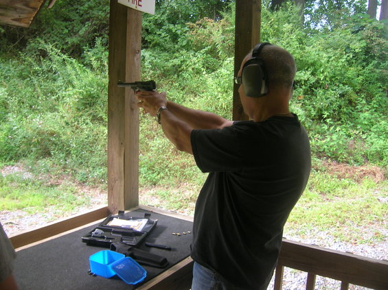 Man wearing ear protection aims a pistol at a shooting range