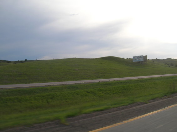 Billboard on a grassy hill with text reading "150 MILES" and "HOT SPRINGS"